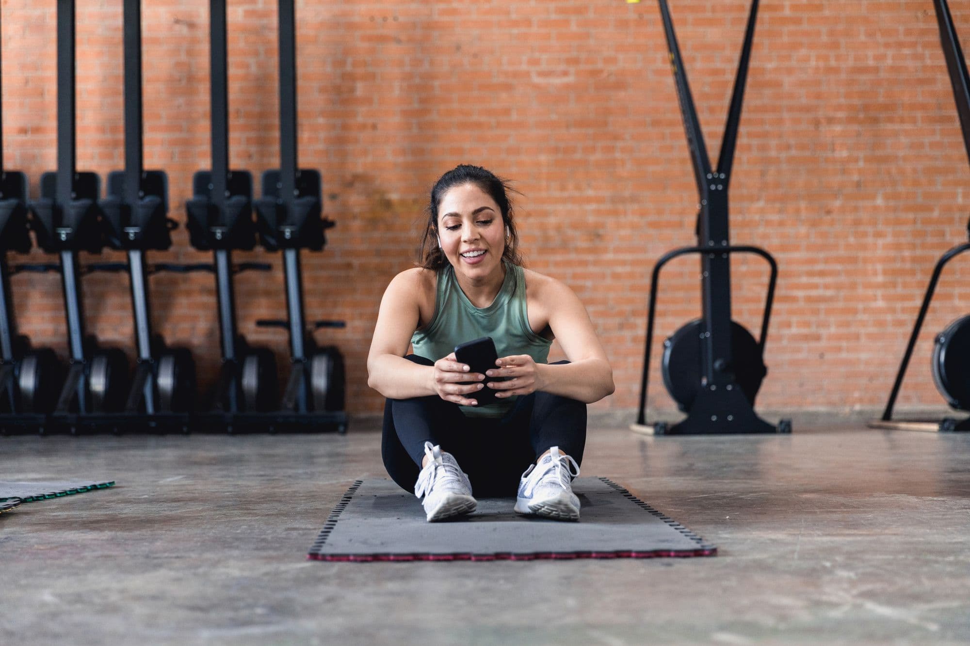 Member sitting on a yoga mat on their phone